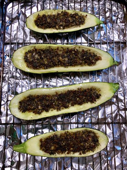Four halved zucchinis with a dark, textured filling are placed on a wire rack over aluminum foil.