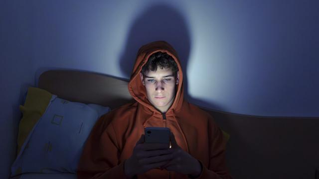 Photo of a teenager using a smartphone lying in bed late at night