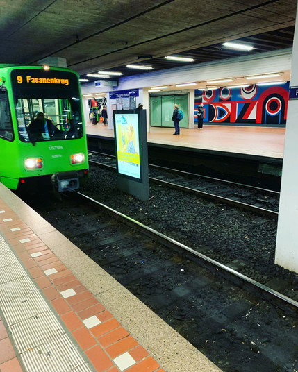 A green Stadtbahn at the Hanover HBF Station, colourful art in the background.