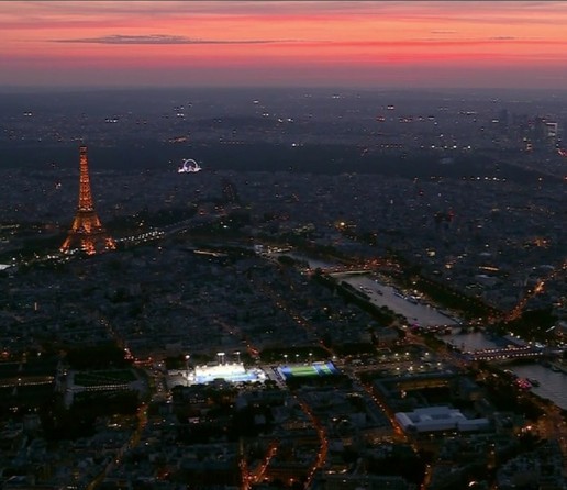 Vista aérea de la ceremonia de apertura de los Juegos Paralímpicos de París. El cielo está coloreado en rosa y naranja por la puesta del sol.