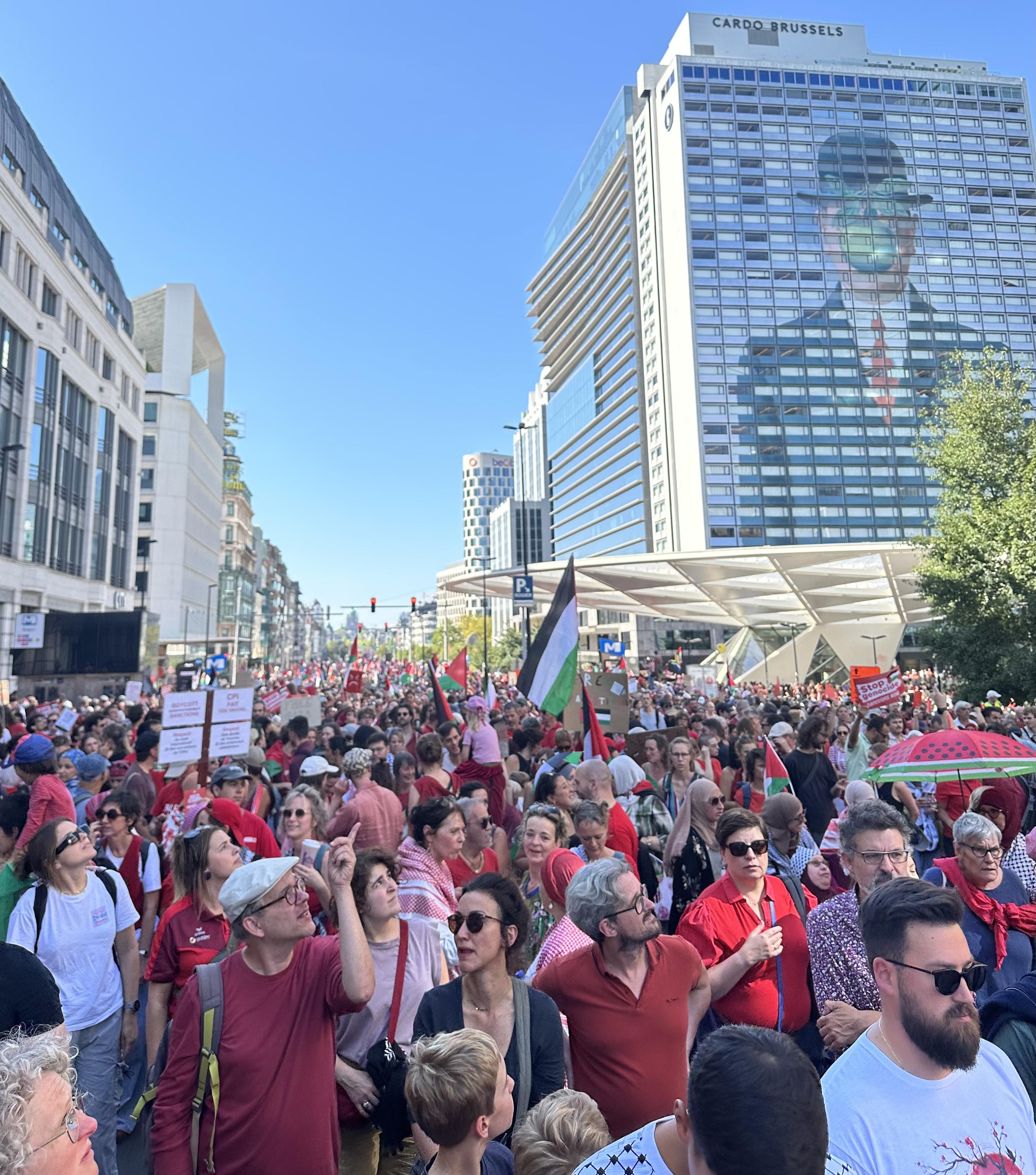 A huge demonstrations for Palestine, with signs, flags and watermelons, stretches into the distance. Magritte’s apple-faced man, painted on a high-rise building, looks on